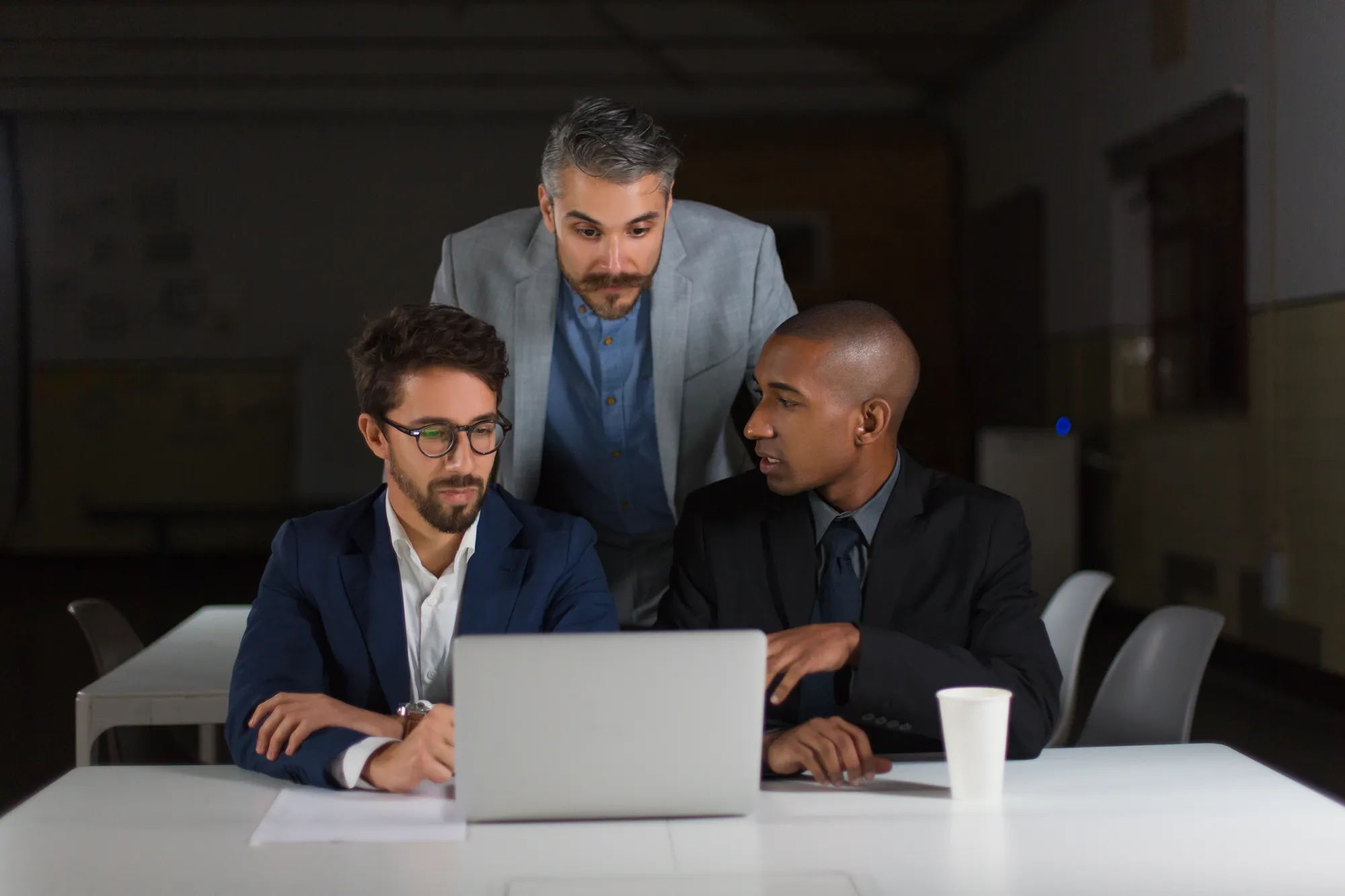Two colleagues reviewing work together on a laptop in a dark office