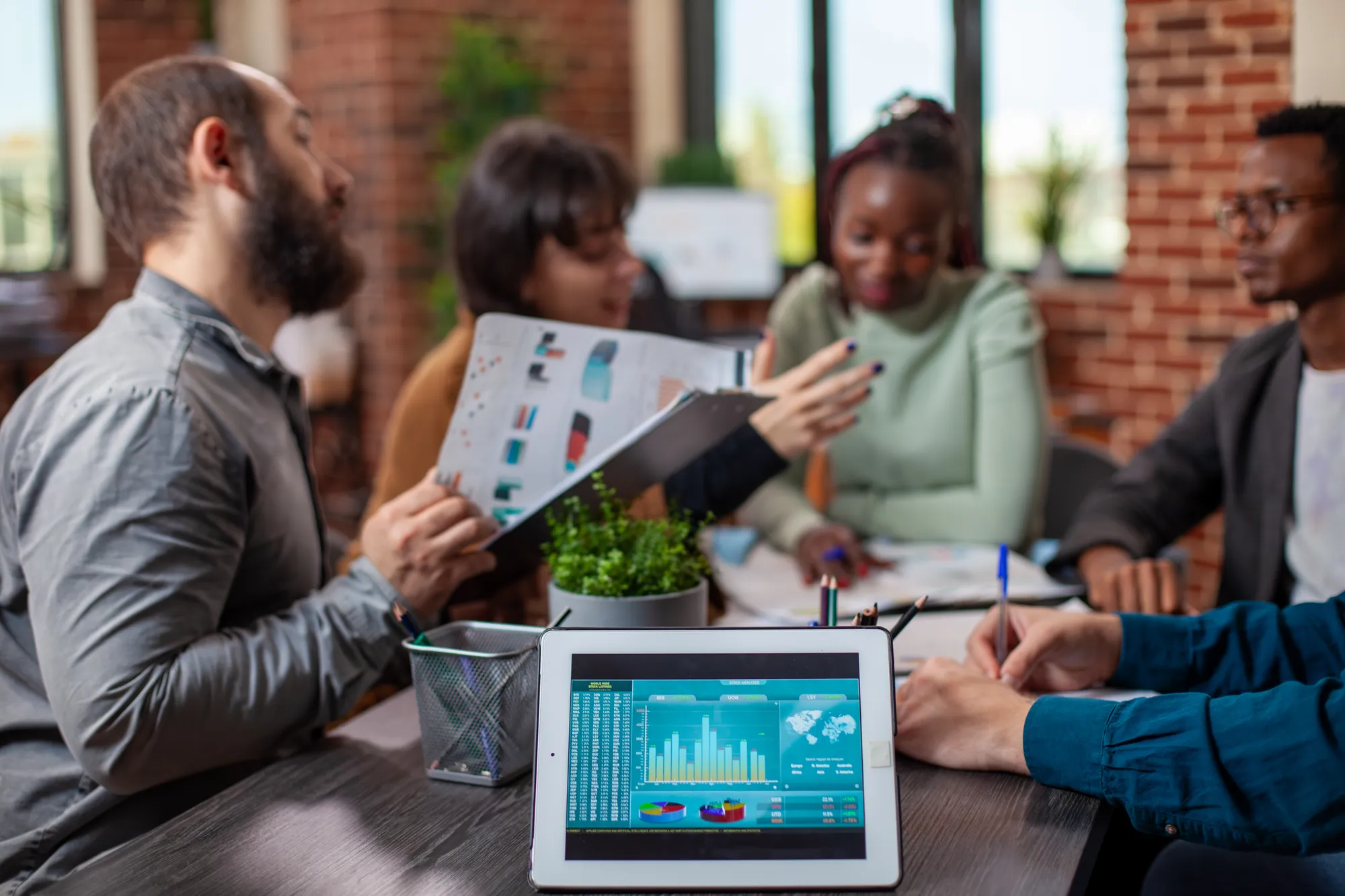 A tablet showing financial charts on a desk while a team talks in the background